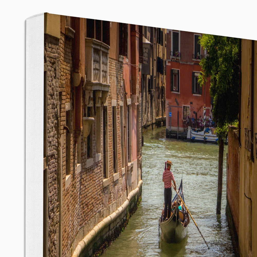 Gondola with gondolier wearing a traditional boater hat and striped top on a  canal in Venice. Italy. Canvas