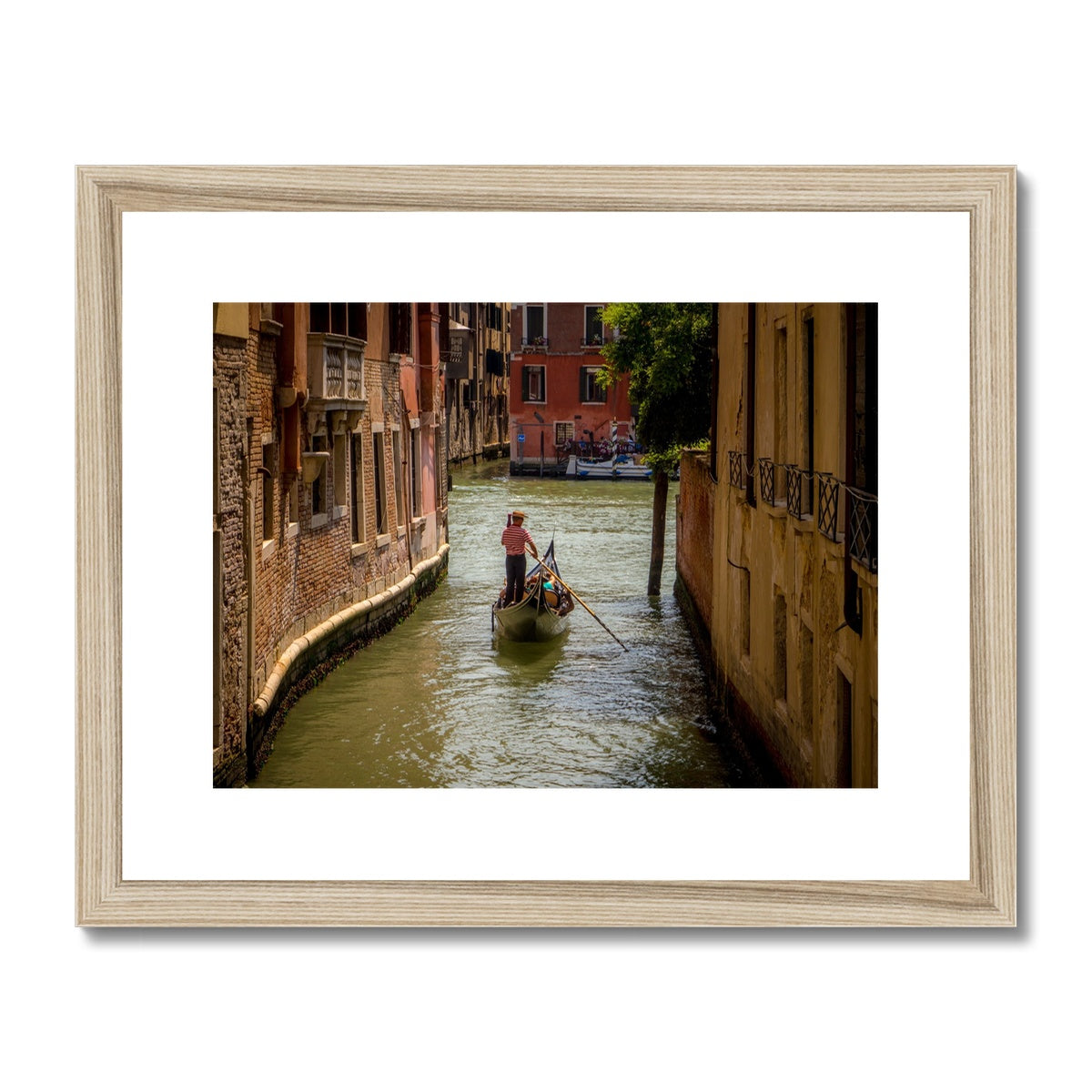 Gondola with gondolier wearing a traditional boater hat and striped top on a  canal in Venice. Italy. Framed & Mounted Print