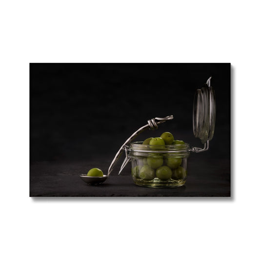 Jar of green olives with single olive on spoon against grey slate background. Canvas