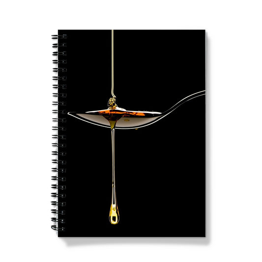 Honey pouring on to metal spoon and dripping off against black background. Notebook