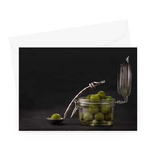 Jar of green olives with single olive on spoon against grey slate background. Greeting Card