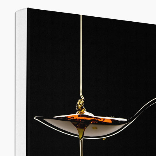 Honey pouring on to metal spoon and dripping off against black background. Canvas