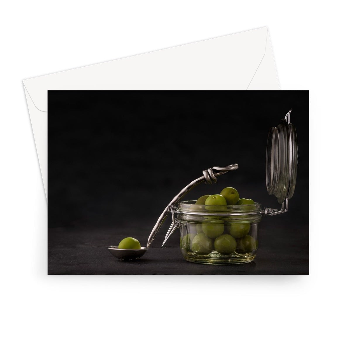 Jar of green olives with single olive on spoon against grey slate background. Greeting Card