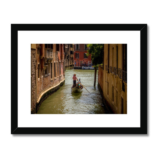 Gondola with gondolier wearing a traditional boater hat and striped top on a  canal in Venice. Italy. Framed & Mounted Print