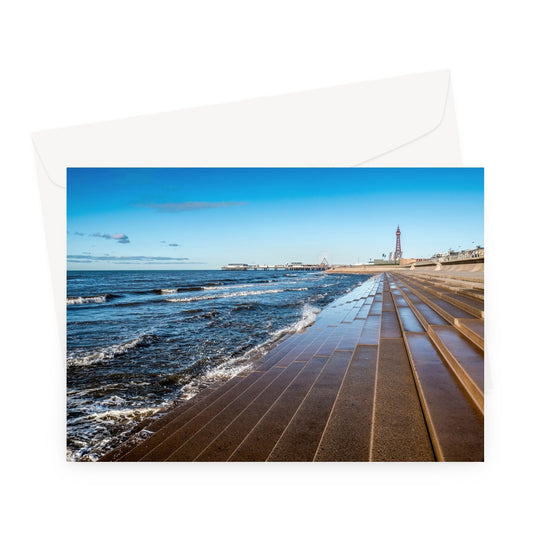 Blackpool's stone stepped sea defences with Blackpool Tower and Central Pier in the distance, Blackpool, UK. Greeting Card