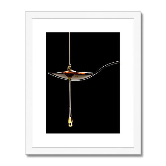 Honey pouring on to metal spoon and dripping off against black background. Framed & Mounted Print