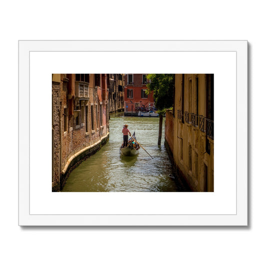 Gondola with gondolier wearing a traditional boater hat and striped top on a  canal in Venice. Italy. Framed & Mounted Print