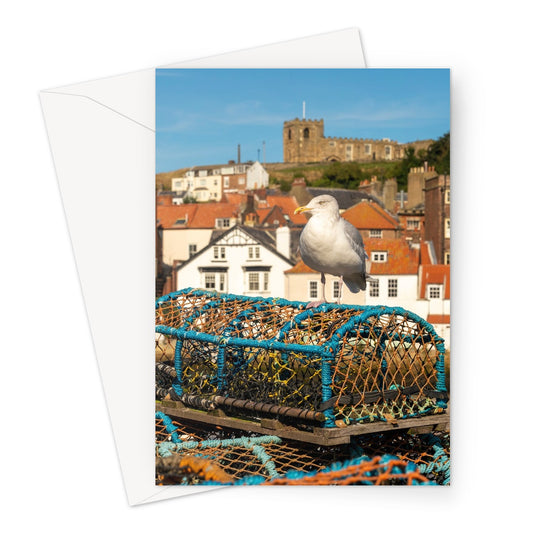 Seagull standing on a lobster trap on the quayside of Whitby harbour with St Mary's church in the distance. Whitby, UK. Greeting Card