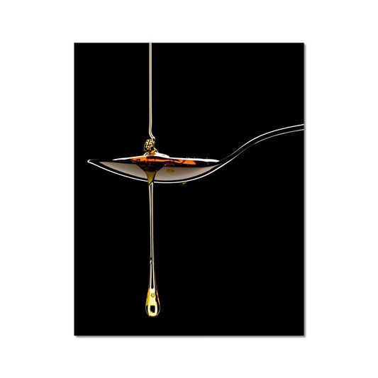 Honey pouring on to metal spoon and dripping off against black background. Fine Art Print