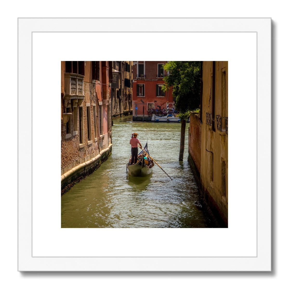 Gondola with gondolier wearing a traditional boater hat and striped top on a  canal in Venice. Italy. Framed & Mounted Print