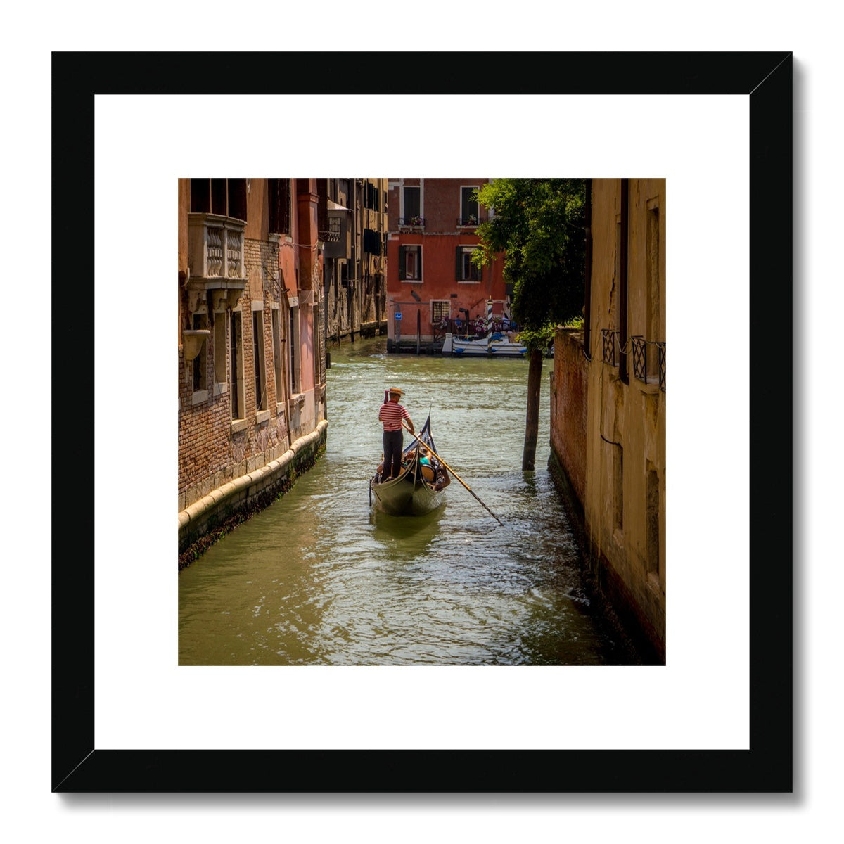 Gondola with gondolier wearing a traditional boater hat and striped top on a  canal in Venice. Italy. Framed & Mounted Print